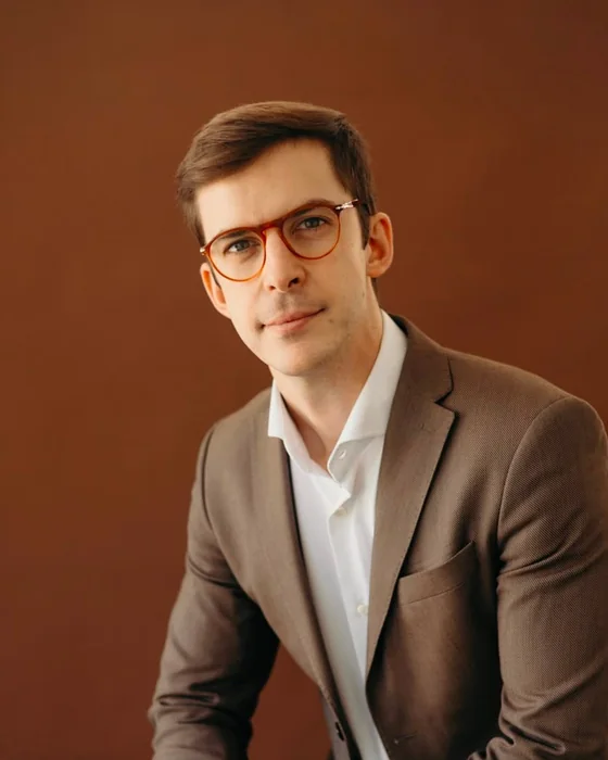 Dr. João Gubert, de óculos e blazer, sentado em estúdio